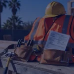 Workers' comp certificate of insurance with California contractor tool belt, hard hat, and safety vest at a residential framing jobsite